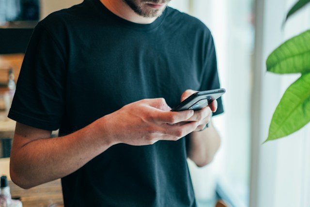 黒いクルーネックトップの男性がスマートフォンを使っている